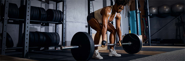 Muscular African American lady lifting the loaded barbell off the ground with both hands